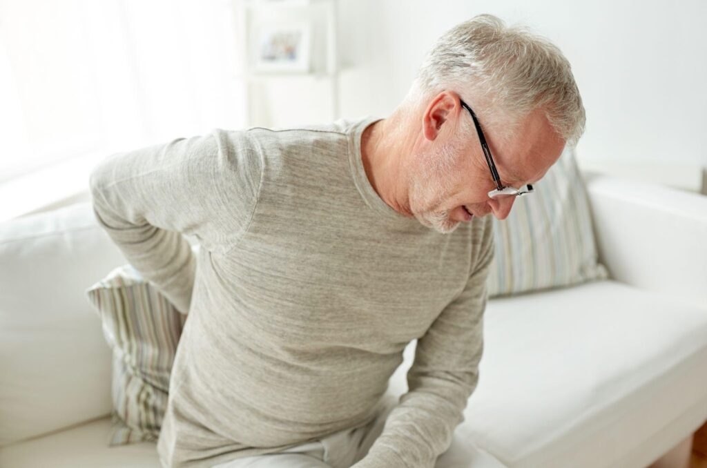 Senior man sitting on a bed and holding his lower back due to discomfort or chronic back pain