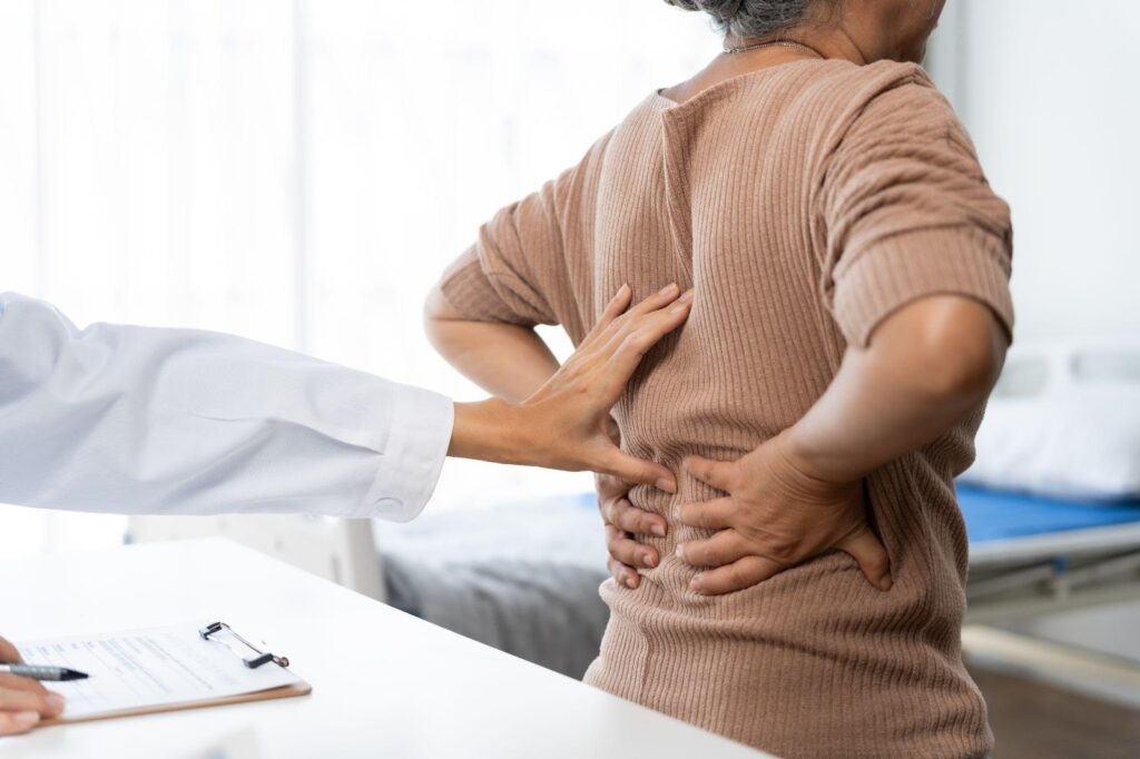 Doctor examining the lower back of an older adult during a medical consultation for chronic back pain