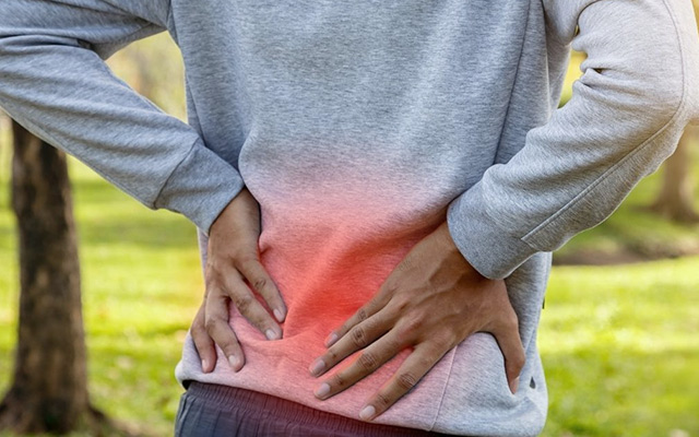 Individual experiencing lower back pain outdoors, highlighting common causes like muscle imbalance and poor posture.